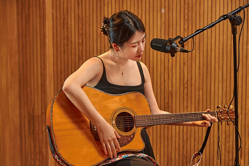 Woman playing acoustic guitar with a microphone setup in a studio.