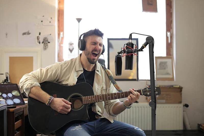 A man recording acoustic guitar, wearing headphones and using a professional microphone setup.