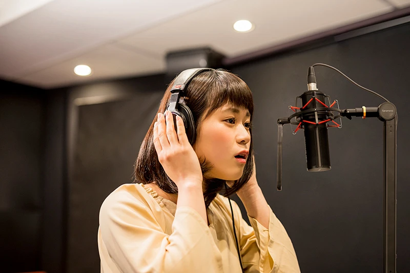 A focused singer wearing headphones preparing to record at a professional microphone in a studio.