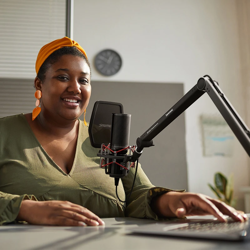 Smiling podcaster with orange headwrap recording with Saramonic microphone in home studio.