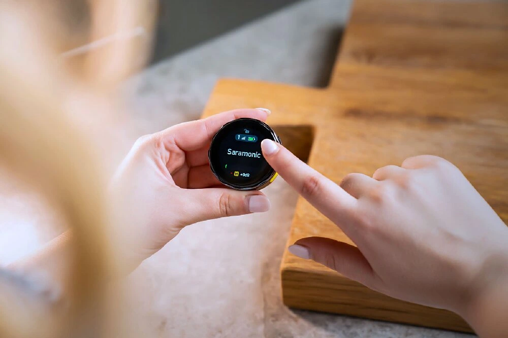 Hands interacting with the touchscreen of a Saramonic wireless microphone unit.