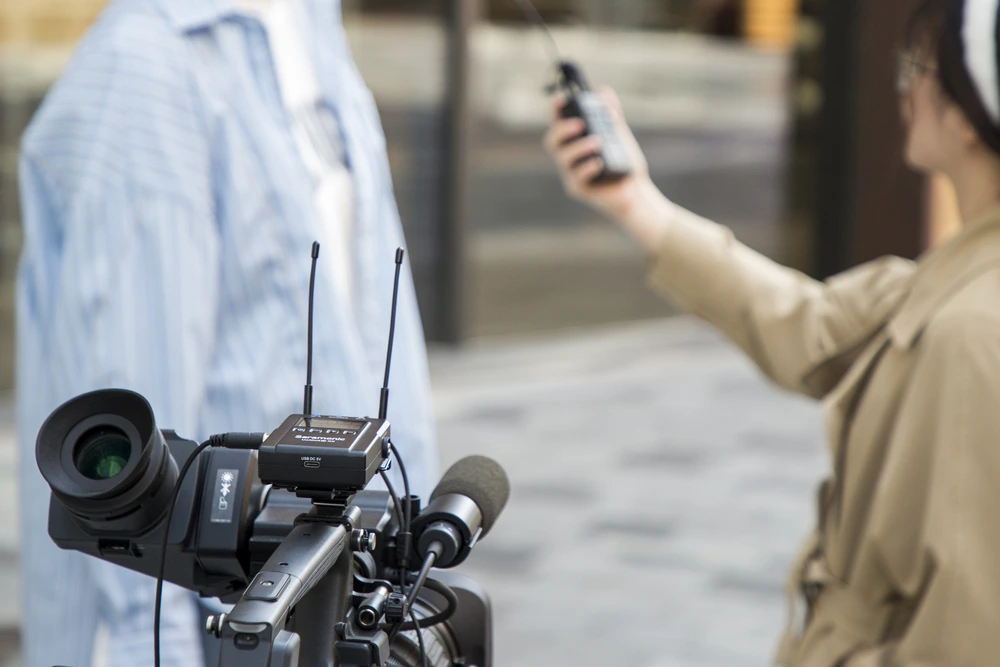 Professional video camera with mounted microphone and wireless receiver for outdoor filming or interview.