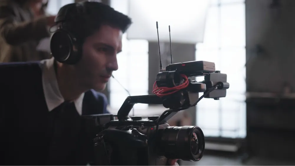 A focused cameraman wearing headphones with an attached microphone operates a professional video camera.