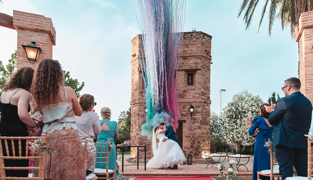 Bride and groom kissing as colorful smoke erupts during their outdoor wedding ceremony