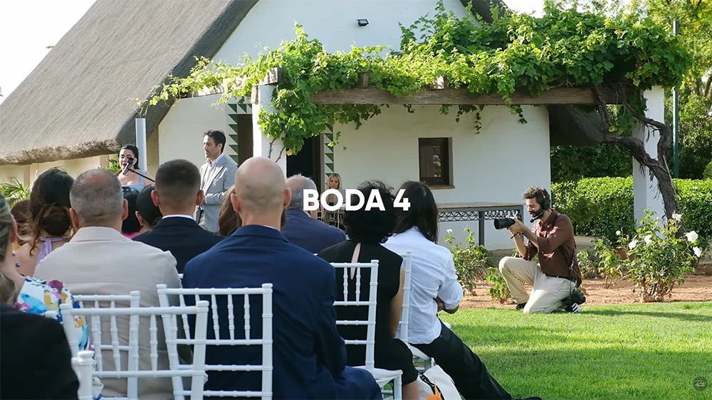 Wedding videographer filming an outdoor ceremony with guests seated nearby